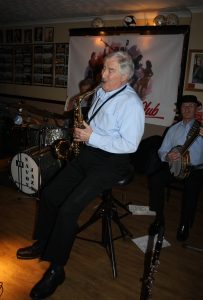 John Crocker plays tenor sax, one of  'Barry Palser's Super Six' at Farnborough Jazz Club (Kent) on 12th February 2016.  Also (hidden) John Tyson on drums and Tony Pitt on banjo. Photo by Mike Witt.