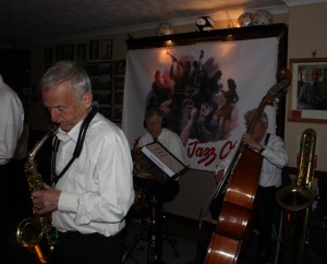 Bernie Holden (alto sax), Chris Welch (drms) and John Bayne (d.bass-with bass sax in front) play in Bob Dwyer's Bix &Pieces at Farnborough Jazz Club on 18th March 2016. Photo by Mike Witt.